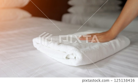 Hotel maid folding white towels on bed 125138416