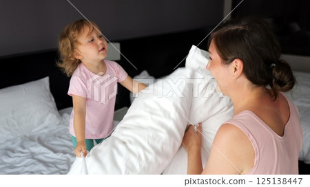 Mother and daughter having pillow fight in hotel room 125138447