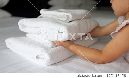 Little girl carefully puts towel onto bed in hotel room 125138458