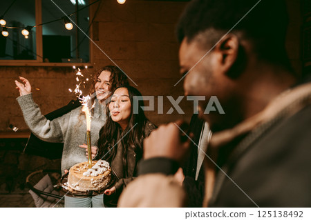 Friends celebrate with a birthday cake and sparklers at an evening gathering outdoors 125138492