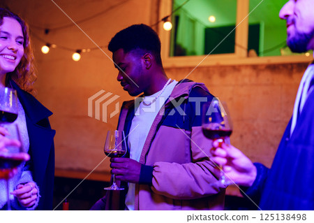 Friends enjoying a lively evening with wine in a cozy venue decorated with string lights 125138498