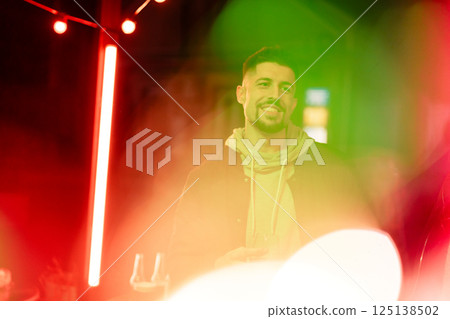 Cheerful man enjoying vibrant nightlife at city bar with colorful lights in the background Cheerful man enjoying vibrant nightlife at city bar with colorful lights in the background 125138502