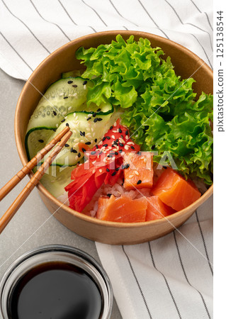 Fresh sushi bowl with salmon, lettuce, and cucumber served in a bamboo dish with chopsticks 125138544