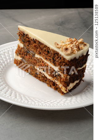 Delightful slice of spiced cake topped with creamy frosting and nuts on a decorative plate 125138589