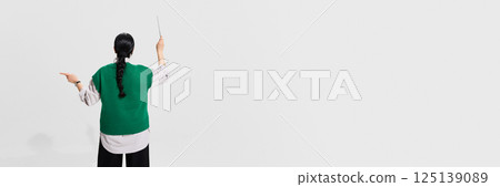 Teacher in green vest stands facing white background with pointer raised, expressing lesson against white studio background. 125139089