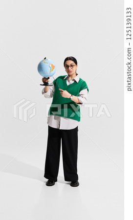 Teacher holding globe and pointer while explaining geography lesson with confident posture. Teacher holding globe and pointer while explaining geography lesson with confident posture. 125139133