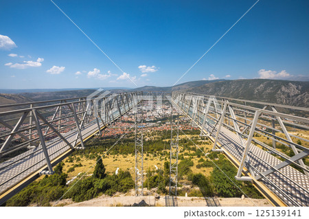 View of Mostar from the Fortica hill, Bosnia and Herzegovina, Europe. Panoramic platform over the city offering views of the cityscape, mountains, and surrounding landscape under a clear blue sky. View of Mostar from the Fortica hill, Bosnia and Herzegovina, Europe. Panoramic platform over the city offering views of the cityscape, mountains, and surrounding landscape under a clear blue sky. 125139141