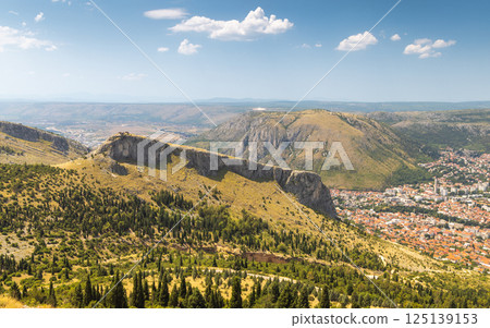 View of Mostar from the Fortica hill, Bosnia and Herzegovina, Europe. Scenic vista of mountainous landscape and sprawling city below a sunny sky. View of Mostar from the Fortica hill, Bosnia and Herzegovina, Europe. Scenic vista of mountainous landscape and sprawling city below a sunny sky. 125139153