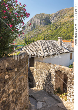 Mostar, historic town in Bosnia and Herzegovina, Europe. Scenic European Townscape: Stone walls and building, with a mountain backdrop under a clear sky. Charming old-world architecture. 125139168