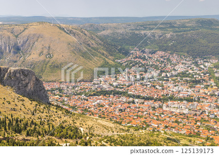 View of Mostar from the Fortica hill, Bosnia and Herzegovina, Europe. Scenic overlook of a city nestled in a valley, showing the urban architecture surrounded by hills and mountains. 125139173