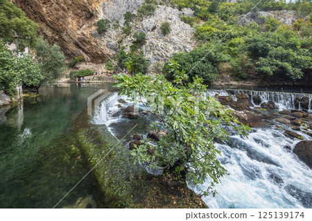 Buna river near the Blagaj Tekke monastery, Bosnia and Herzegovina, Europe. Scenic waterfall cascading through a verdant landscape, creating a tranquil and picturesque natural setting. Buna river near the Blagaj Tekke monastery, Bosnia and Herzegovina, Europe. Scenic waterfall cascading through a verdant landscape, creating a tranquil and picturesque natural setting. 125139174