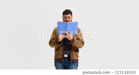 Man in glasses, teacher reading blue book with full attention against white background. 125139193
