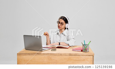 Focused female teacher in white shirt and headphones explaining subject during online lesson with expressive gesture. 125139198