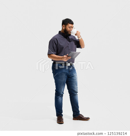 Focused male professional sipping coffee while reading tablet, representing balance between routine, knowledge absorption and digital learning Focused male professional sipping coffee while reading tablet, representing balance between routine, knowledge absorption and digital learning 125139214