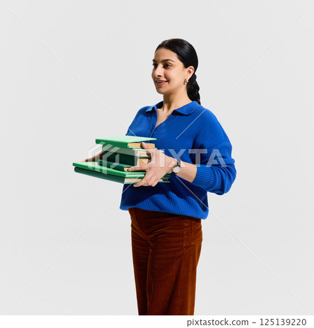 Side view of female teacher walking with stack of green books and confident smile, portraying motivation, academic progress 125139220
