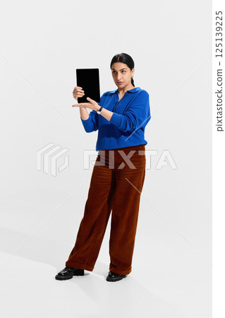 Serious woman, teach in blue holding tablet with both hands, demonstrating digital presentation skills and e-learning opportunities. Serious woman, teach in blue holding tablet with both hands, demonstrating digital presentation skills and e-learning opportunities. 125139225