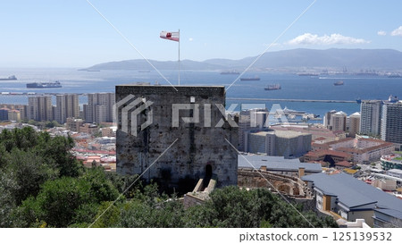 Moorish Castle tower with Gibraltar flag waving in the wind, blue sky and sea in background 125139532