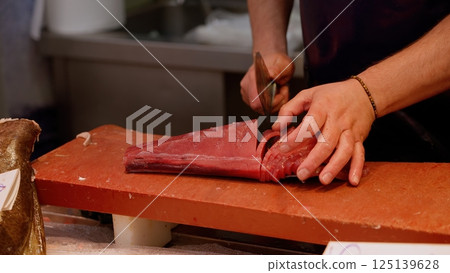 Fishmonger slicing fresh tuna fillet on cutting board 125139628