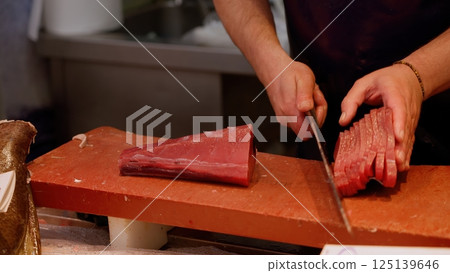 Fishmonger slicing fresh tuna fillet on cutting board 125139646
