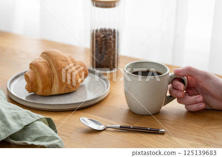 Hand holding a cup of freshly brewed coffee on a wooden table with croissants 125139683
