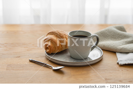 Cup of coffee espresso and croissant on a plate on a wooden table with napkin 125139684