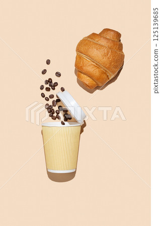 Paper cup with scattered coffee beans and fresh croissant on yellow isolated background 125139685
