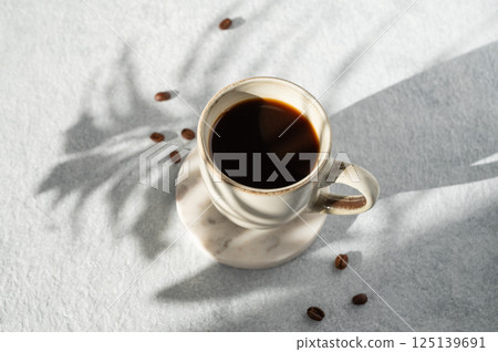 Cup of freshly brewed coffee on light textured background with shadow of leaf 125139691