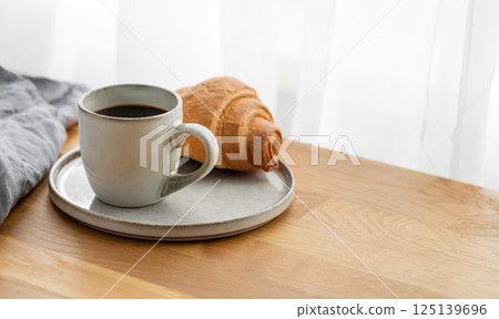 Cup of freshly brewed coffee and croissant on a plate on a wooden table 125139696