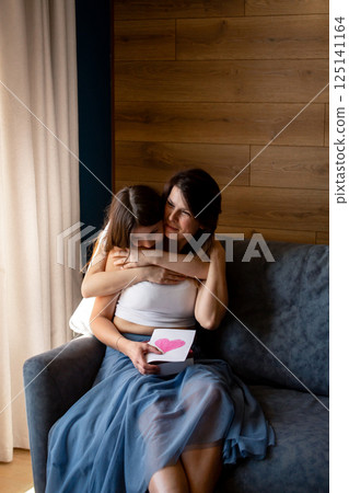 Happy mother's day. Preteen daughter hugs and congratulates moms giving her gift box. Motherhood concept. 125141164