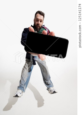 Young man leans forward, presenting smartphone with blank screen against white studio background. Young man leans forward, presenting smartphone with blank screen against white studio background. 125141174