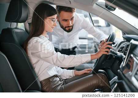 Checking the salon of automobile. Man with woman in white clothes are in the car dealership together Checking the salon of automobile. Man with woman in white clothes are in the car dealership together 125141200