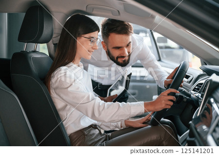 Woman sitting in the automobile. Man in white clothes are in the car dealership Woman sitting in the automobile. Man in white clothes are in the car dealership 125141201