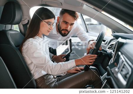Woman sitting in the automobile. Man in white clothes are in the car dealership Woman sitting in the automobile. Man in white clothes are in the car dealership 125141202