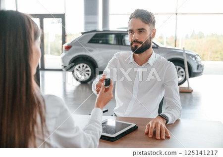Automobile keys for the new owner. Man with woman in white clothes are in the car dealership together Automobile keys for the new owner. Man with woman in white clothes are in the car dealership together 125141217