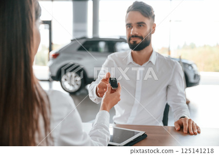 Automobile keys for the new owner. Man with woman in white clothes are in the car dealership together 125141218