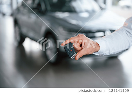 Close up view of keys that are in hand. Young man in white clothes is in the car dealership 125141309