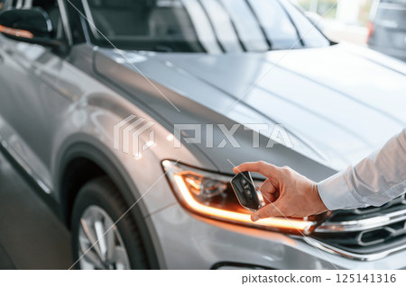 Keys and remote controller. Close up view. Young man in white clothes is in the car dealership 125141316