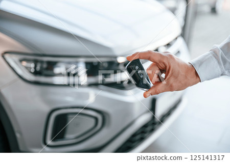 Keys and remote controller. Close up view. Young man in white clothes is in the car dealership 125141317