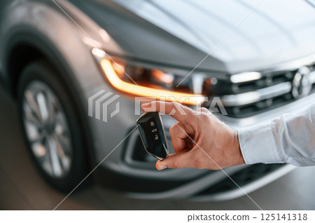 Keys and remote controller. Close up view. Young man in white clothes is in the car dealership 125141318