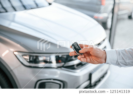 Keys and remote controller. Close up view. Young man in white clothes is in the car dealership 125141319