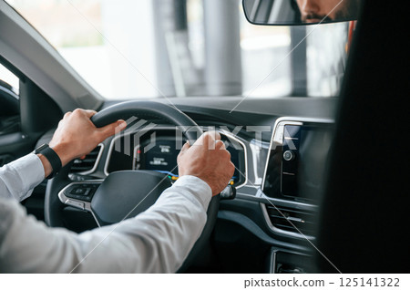 Test drive. Young man in white clothes is in the car dealership 125141322