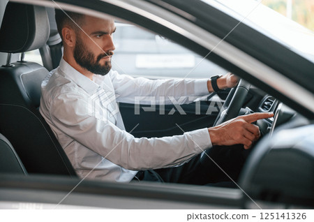 Test drive. Young man in white clothes is in the car dealership 125141326