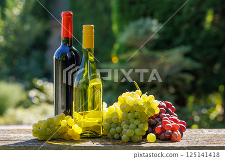 A basket filled with various types of grapes and bottles of red and white wine 125141418