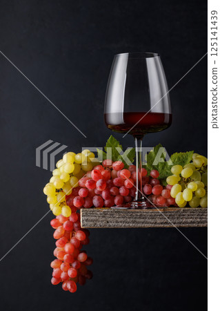 A glass of wine paired with grapes, set against a dark background A glass of wine paired with grapes, set against a dark background 125141439