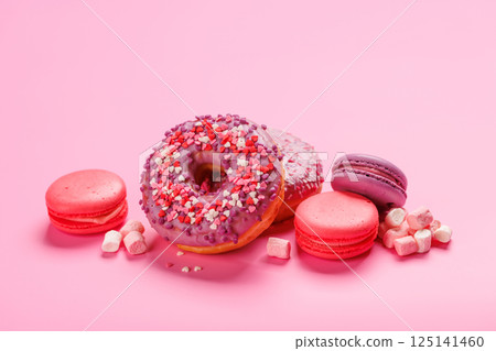 An eye-catching arrangement of colorful macarons and donuts on a pastel pink background 125141460