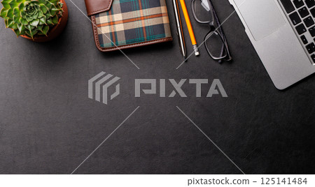 Top view of a dark leather office desk with laptop, supplies, and coffee cup Top view of a dark leather office desk with laptop, supplies, and coffee cup 125141484