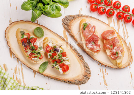 Tasty antipasto toasts featuring classic caprese with mozzarella and tomatoes, and savory prosciutto with herbs 125141502