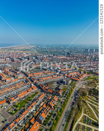 A stunning aerial view of a coastal town with red-tiled rooftops, neatly aligned houses, and a vast sandy beach stretching into the distance under a clear blue sky. A stunning aerial view of a coastal town with red-tiled rooftops, neatly aligned houses, and a vast sandy beach stretching into the distance under a clear blue sky. 125141529