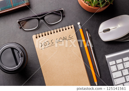 Elegant leather desk setup with laptop, coffee, stationery, and a notepad labeled 2025 Goals 125141561