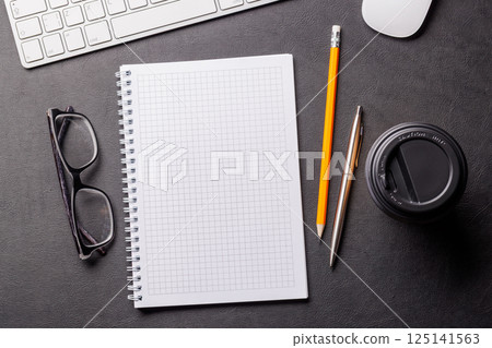 Top view of a dark leather office desk with notepad, supplies, and coffee cup 125141563